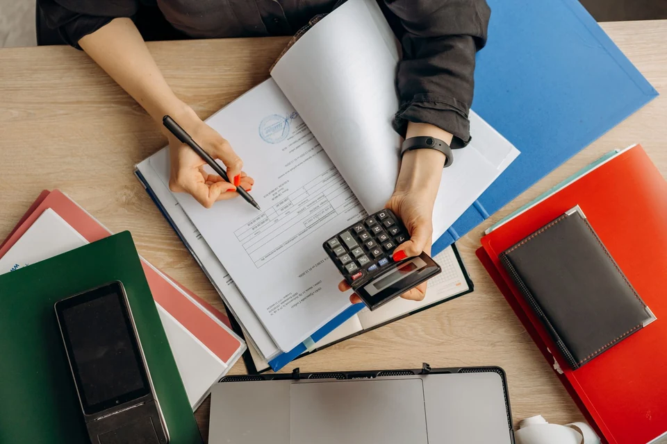 Hands reviewing financial documents beside a calculator and laptop.