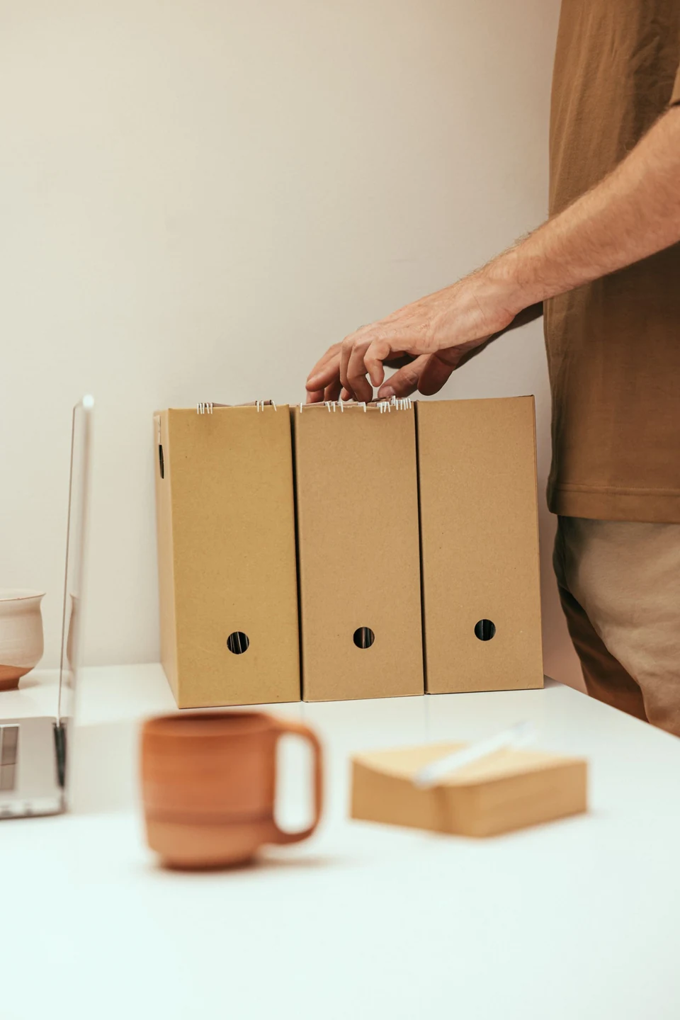 Hands arranging documents in a file organizer beside a laptop and coffee.