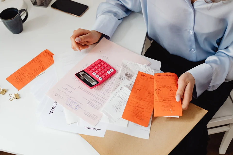 Hands holding paper receipts and checking expenses with a calculator.