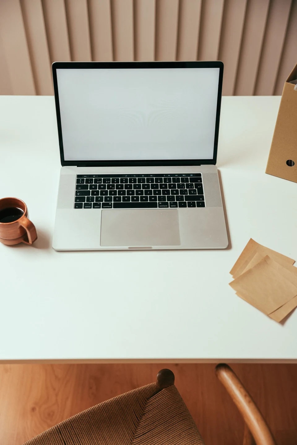 A laptop, coffee and paper in a quiet neutral workspace.