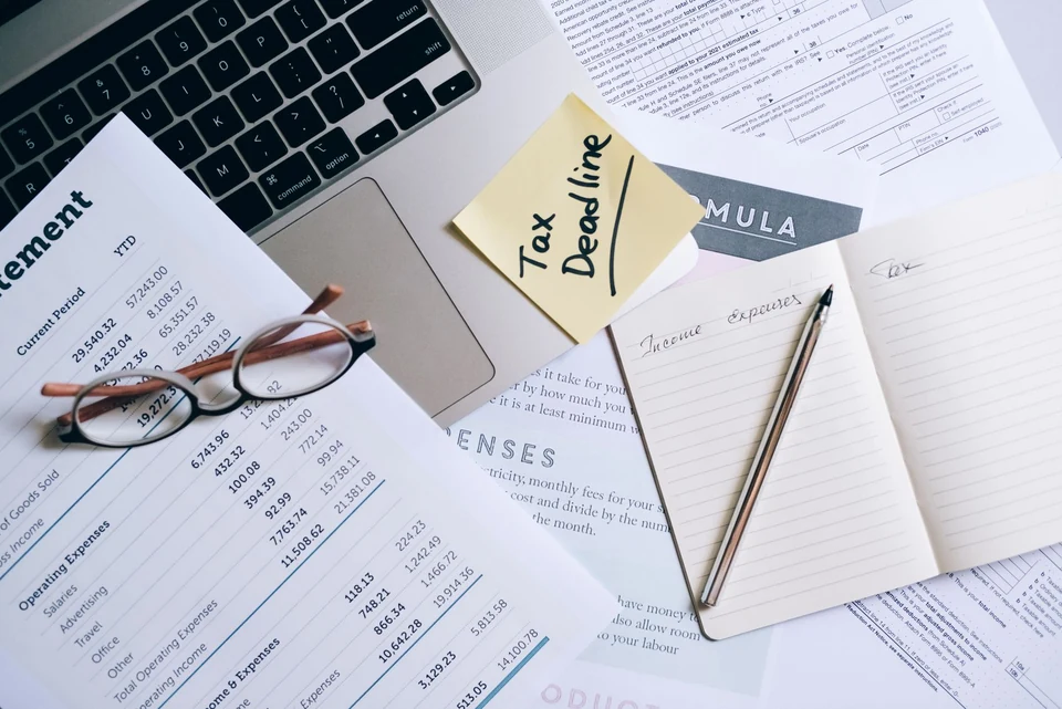 A laptop, notebook and printed financial documents on a working desk.